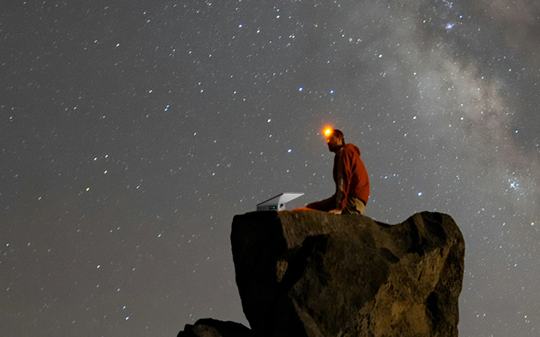 A camper sitting on a rock under the night sky with a Starlink Mini and external battery, showing portable satellite internet and long-lasting power for outdoor adventures.