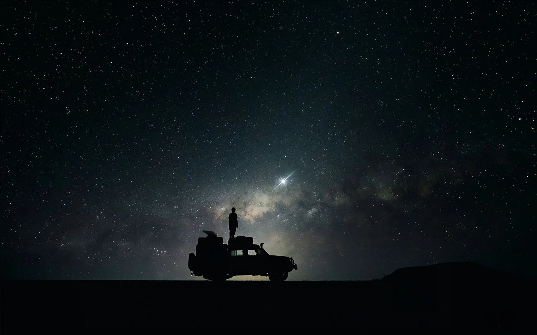 Nighttime scene of a person using Starlink Mini with an external battery while stargazing, illustrating portable internet and power for remote trips